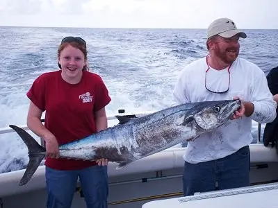Two anglers holding a kingfish on an offshore boat