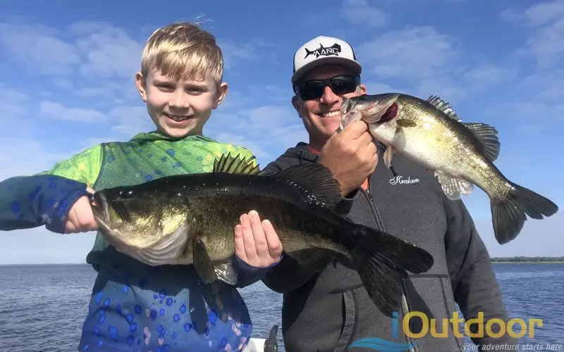 Boy and an adult holding largemouth bass on a boat