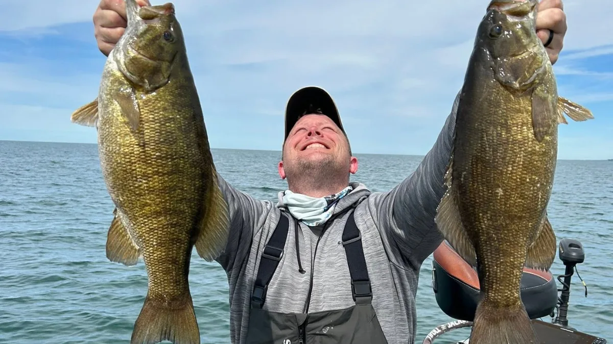 Erie PA Fishing Charters: Smiling angler holding a large smallmouth bass on open water
