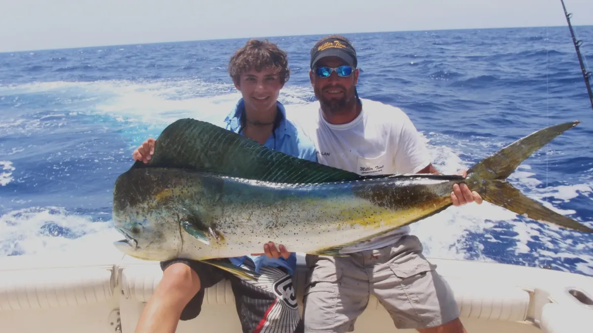 Two anglers holding a big mahi-mahi on a boat