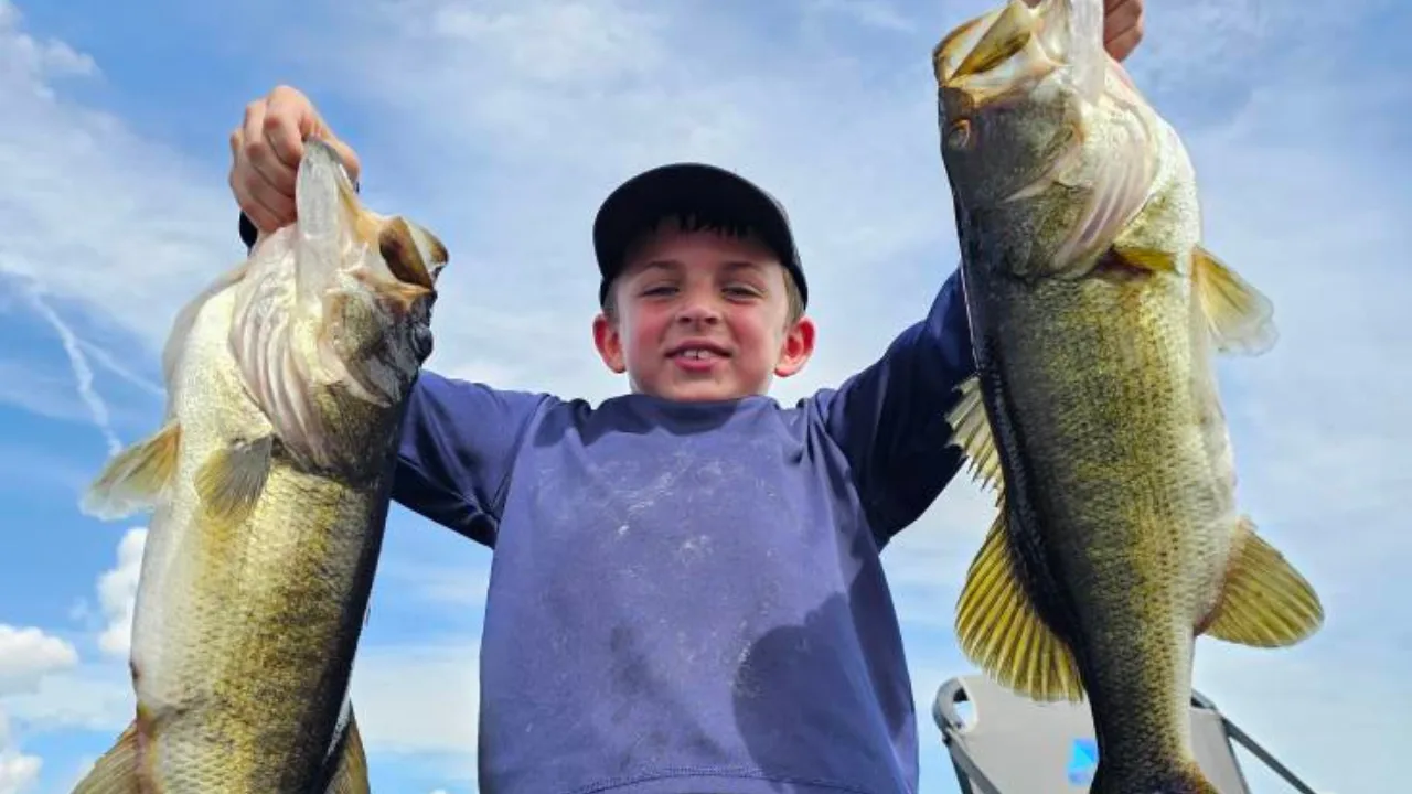 Young angler holding up two largemouth bass on a Headwaters Lake bass trip