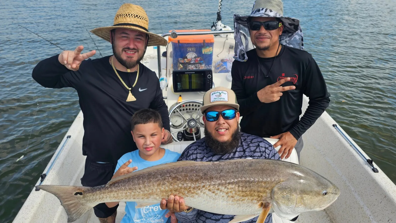 Anglers and a young boy holding a large redfish on a flats boat