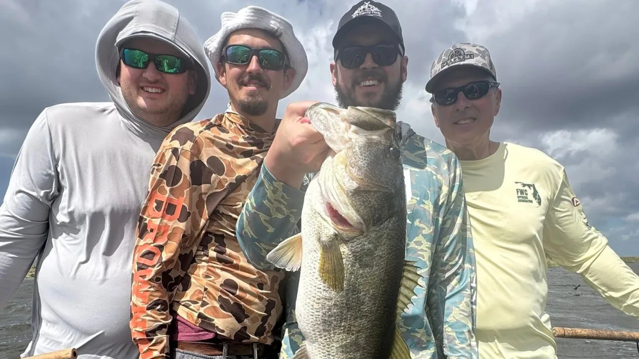 Four anglers on a boat, two holding largemouth bass